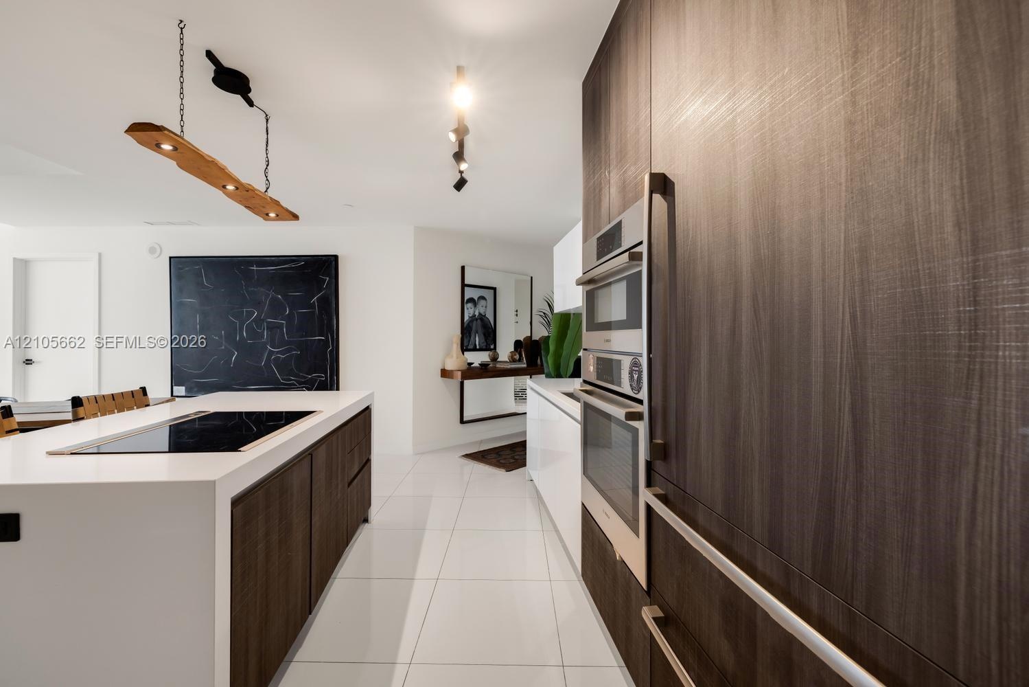 Kitchen featuring full-height wood-finish cabinetry, built-in double wall ovens, a large island with a surface-integrated cooktop, and large-format po