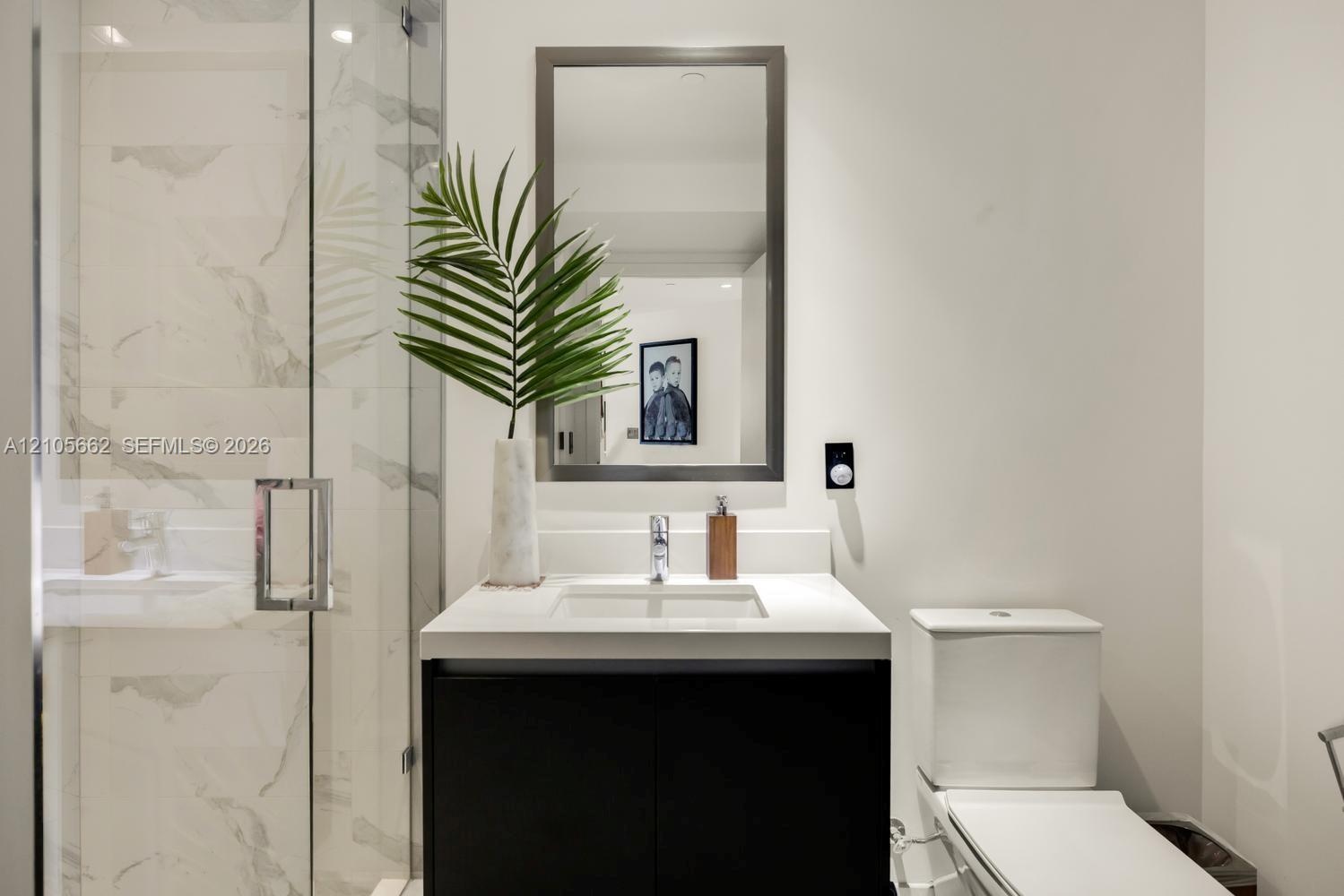 Modern vanity with a countertop basin and cabinet storage, framed wall mirror, glass-enclosed shower with large-format tile surround, and dual-flush t