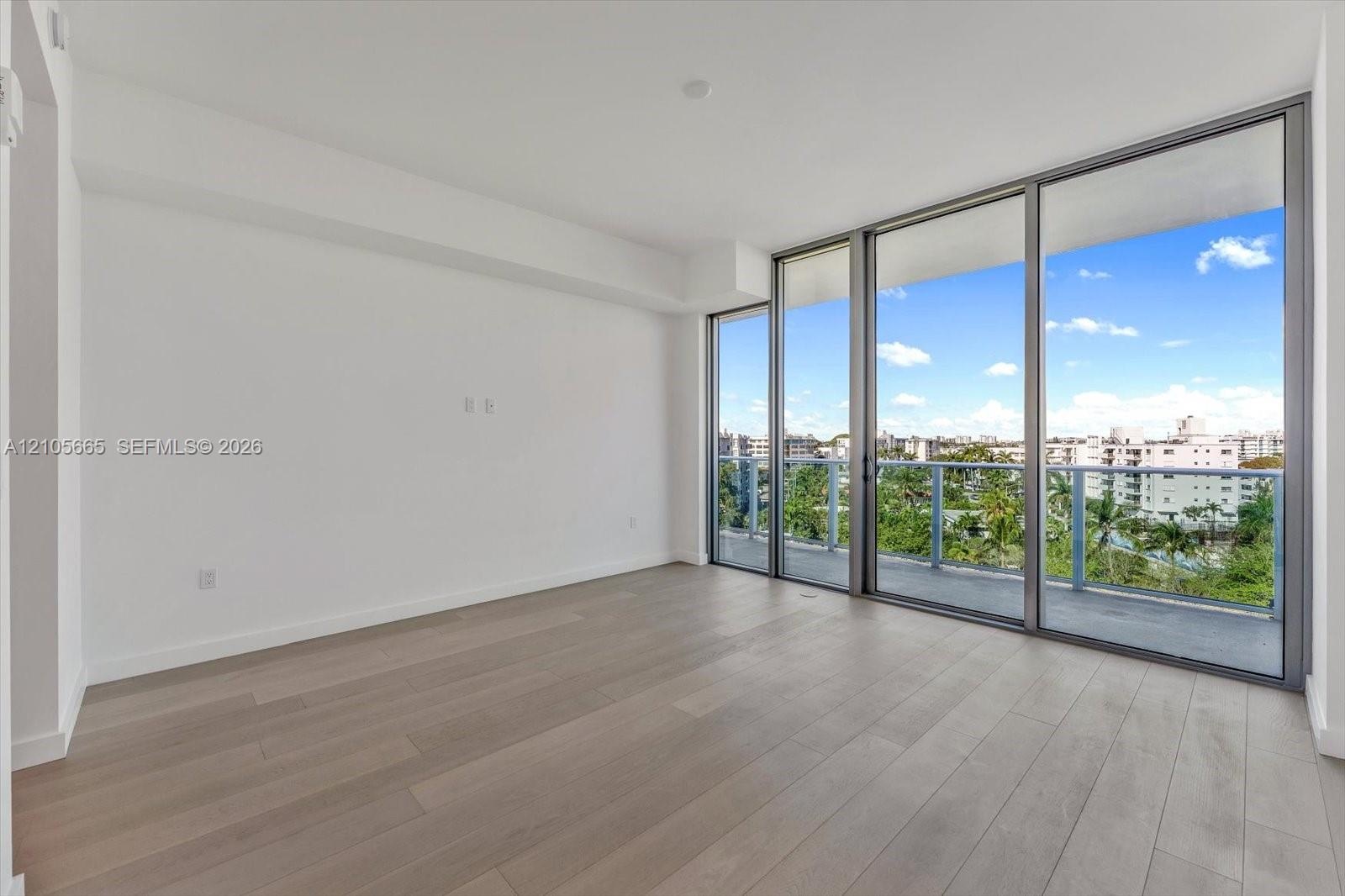 Living area featuring light-toned wood-finish flooring, floor-to-ceiling glass panels, and an outdoor balcony with metal railings