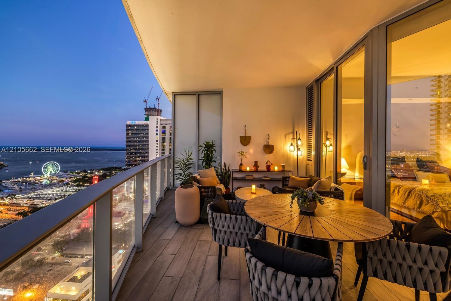 Covered balcony featuring wood-finish flooring, glass panel railings, floor-to-ceiling glass wall, and exterior lighting