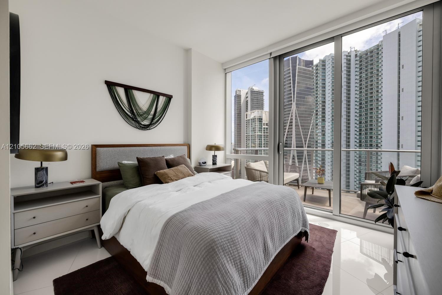 Floor-to-ceiling windows, polished light-toned tile flooring, and a private balcony featuring a glass-railing system