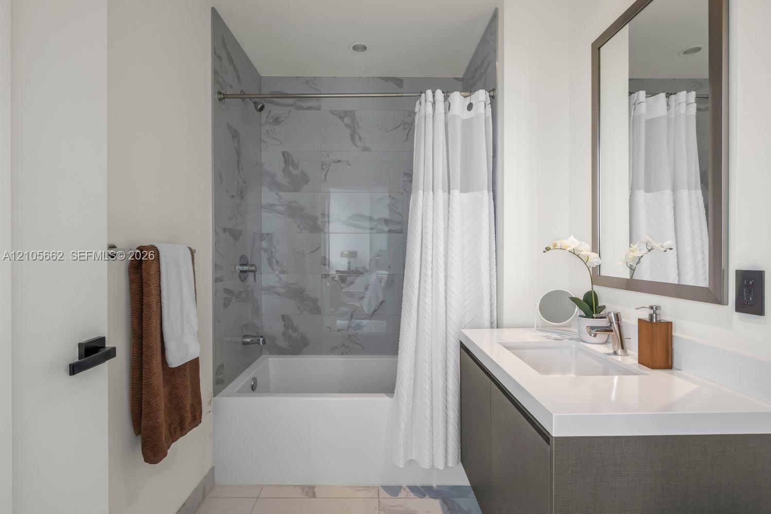Wall-mounted floating vanity with integrated rectangular sink and solid surface countertop, mirror with framed border, and bathtub featuring patterned