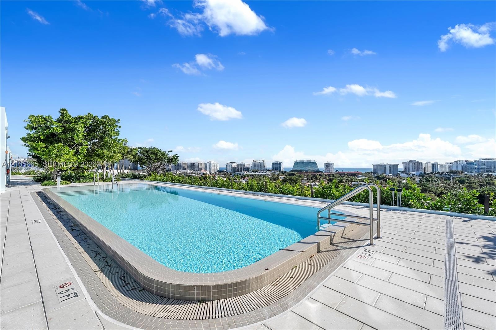 Rooftop swimming pool featuring a tiled deck, integrated metal safety railing, and encompassing urban and coastal scenery