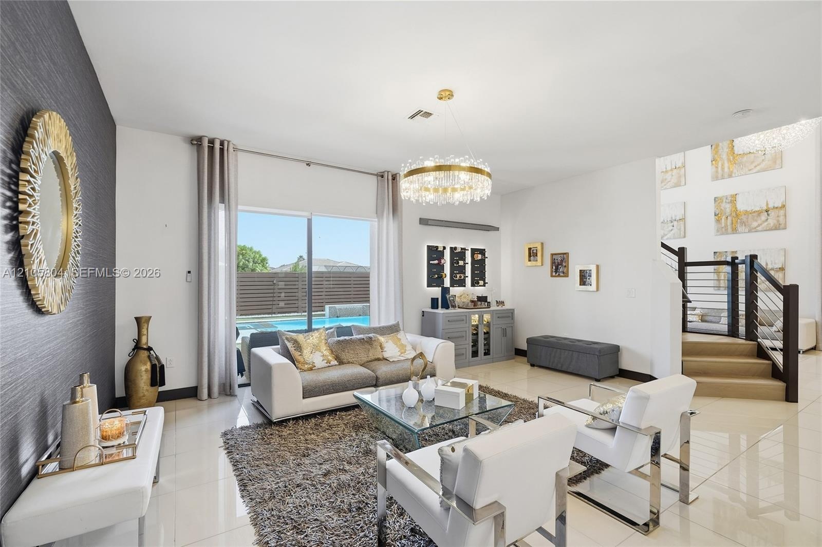 Living area featuring large-format tile flooring, a circular tiered crystal chandelier, a built-in cabinetry unit with integrated lighting, and a stai