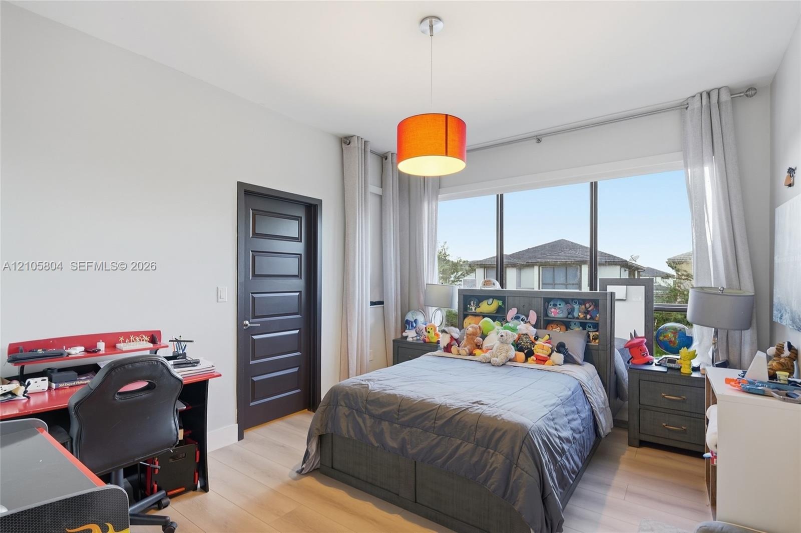 Room featuring wood-finish flooring, a large multi-pane window, and a dark-finished five-panel interior door with a brushed-metal lever handle