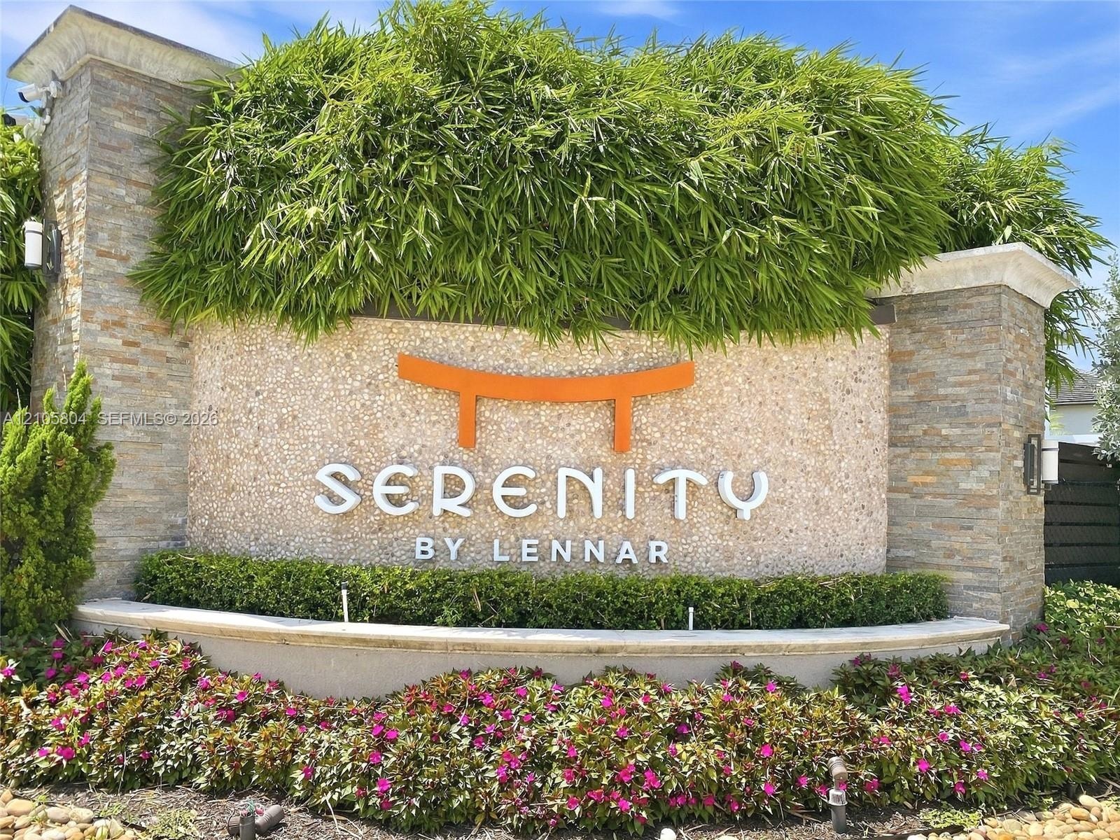 Community entrance sign featuring stacked stone columns, textured masonry, tiered landscaping, and metal accent lighting