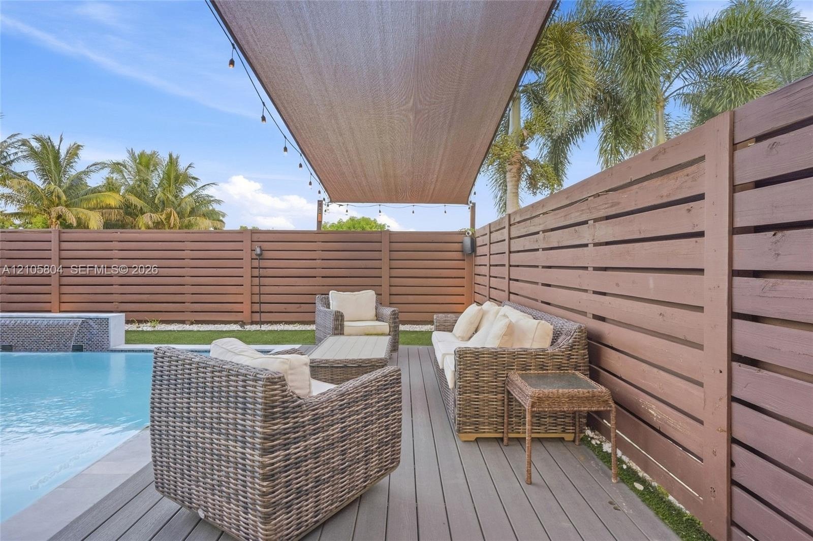 Swimming pool with water feature, composite decking, horizontal wood privacy fencing, and an overhead fabric shade canopy