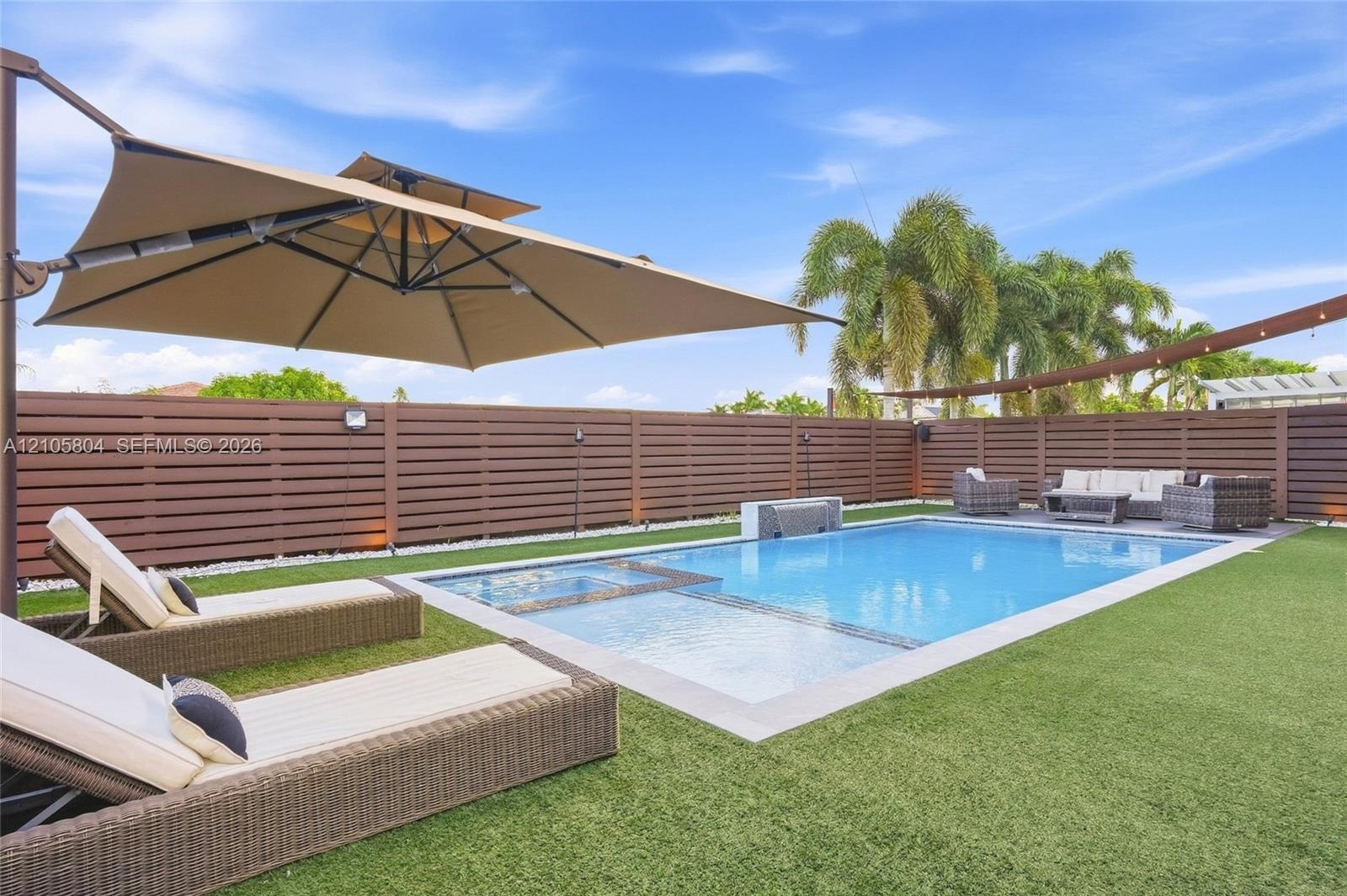 Backyard featuring a rectangular swimming pool with an integrated spa, horizontal slat privacy fencing, artificial turf, and a water feature