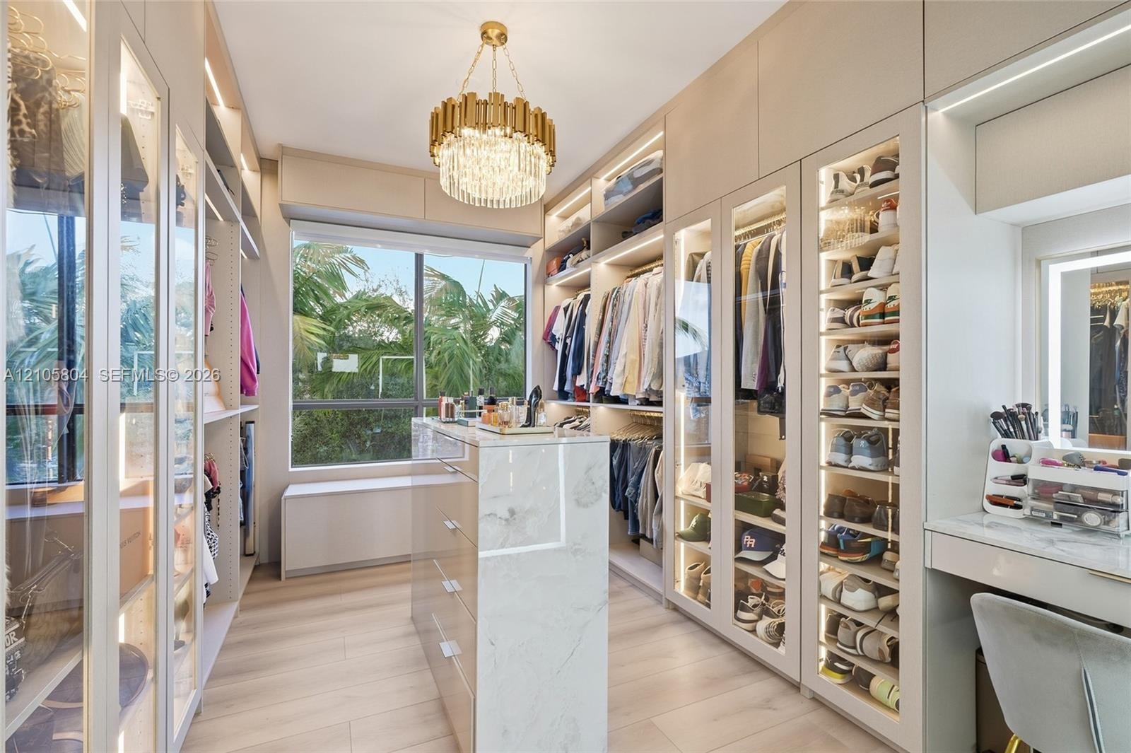 Custom walk-in closet featuring floor-to-ceiling glass-front cabinetry, integrated LED lighting, stone-finish center island, light wood-finish floorin