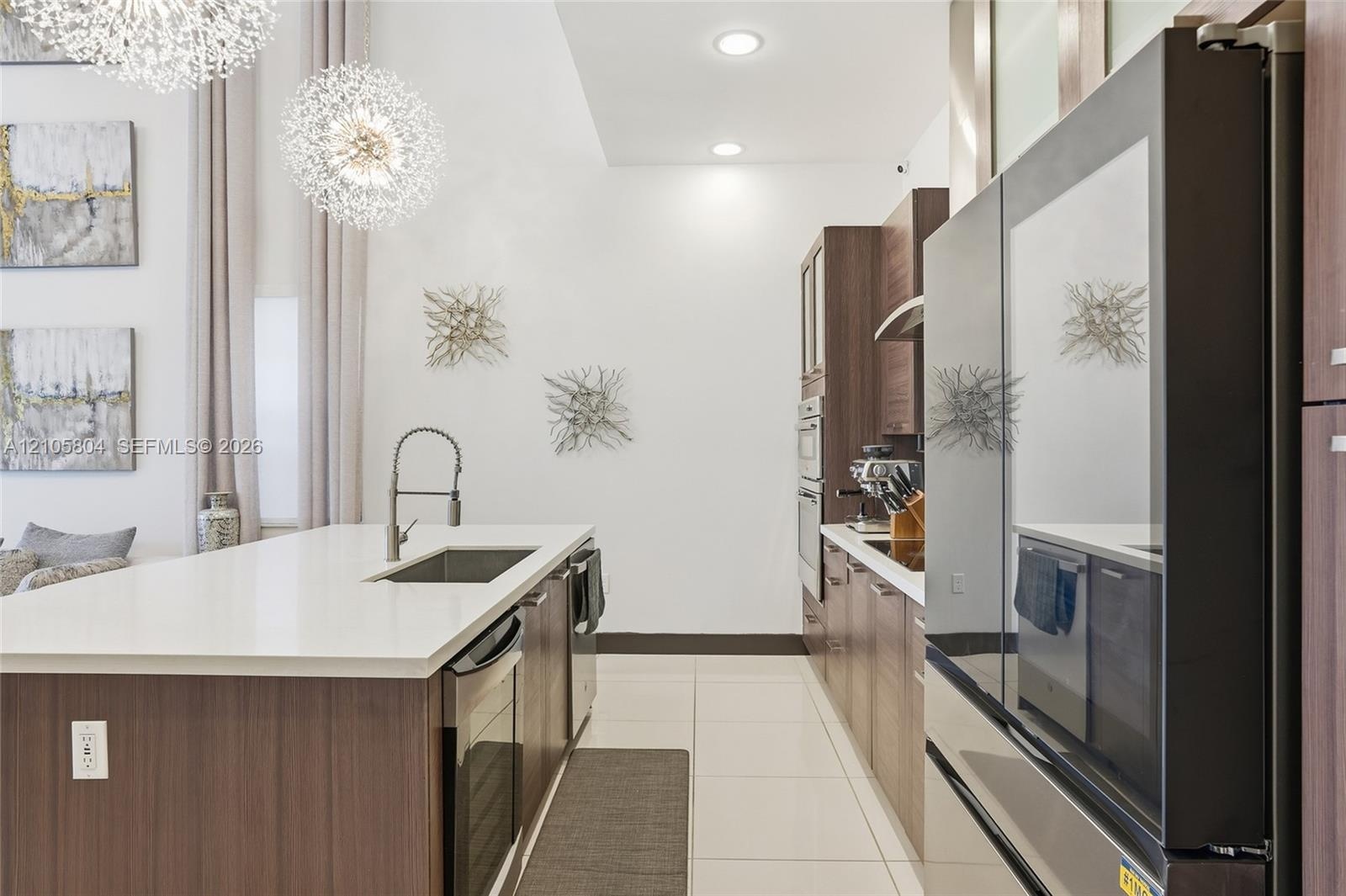 Kitchen featuring a waterfall-edge island with a quartz countertop, flat-panel cabinetry, high-ceiling drum pendant lighting, and stainless steel buil
