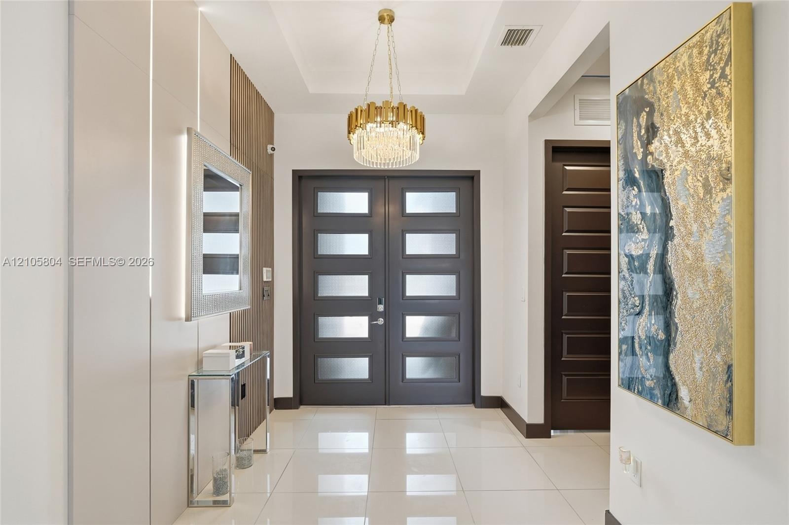 Entryway featuring a double-door entrance with frosted glass panels, tile flooring, a tiered crystal chandelier, and integrated wall paneling with rec