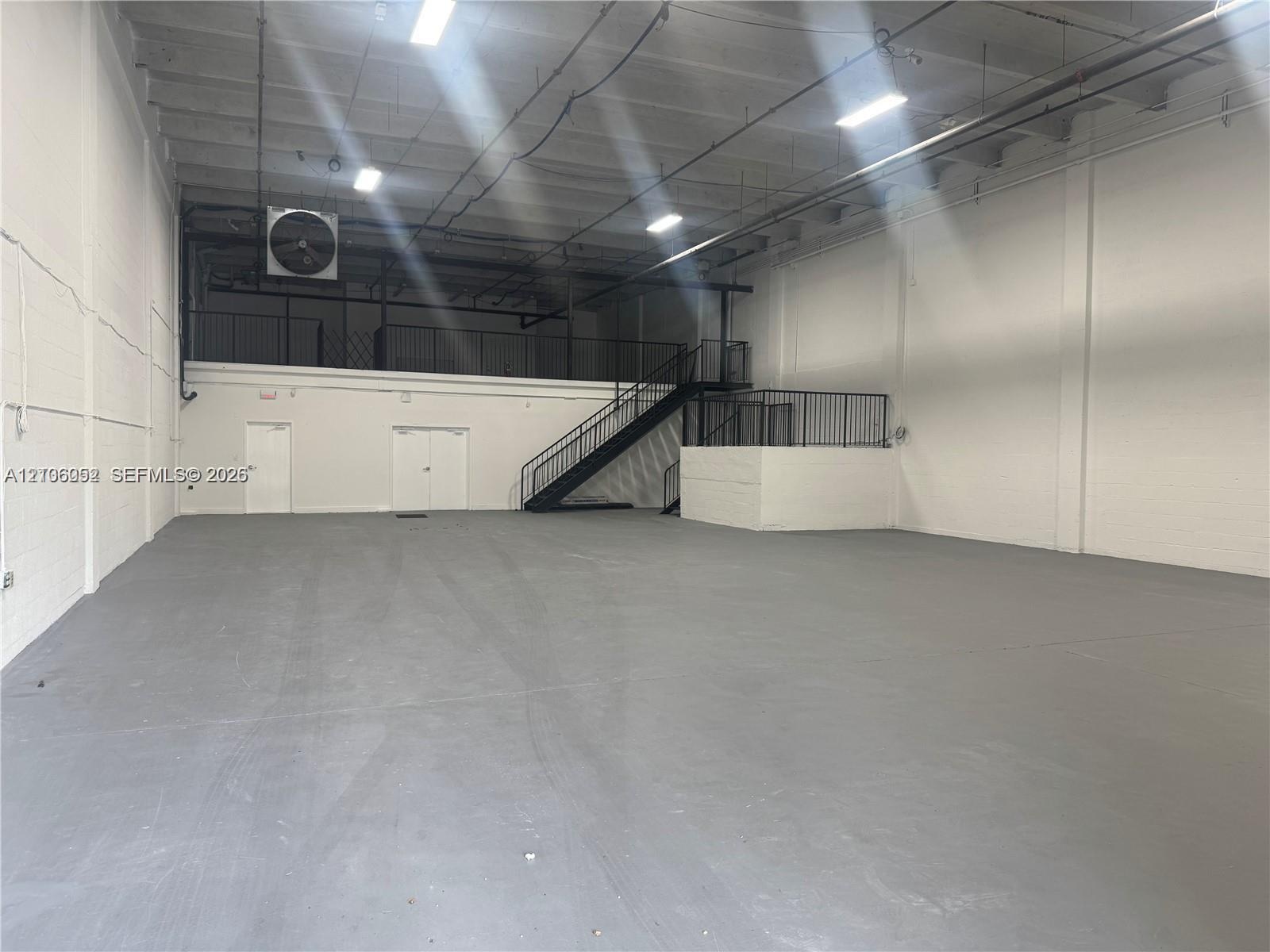 Open-concept industrial warehouse space featuring high ceilings, painted masonry walls, durable floor surfacing, mezzanine level with metal railing, a