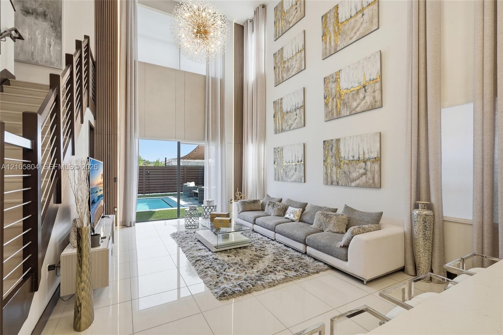 Double-height ceilings featuring floor-to-ceiling windows, polished tile flooring, a statement chandelier, and a staircase with a horizontal cable rai