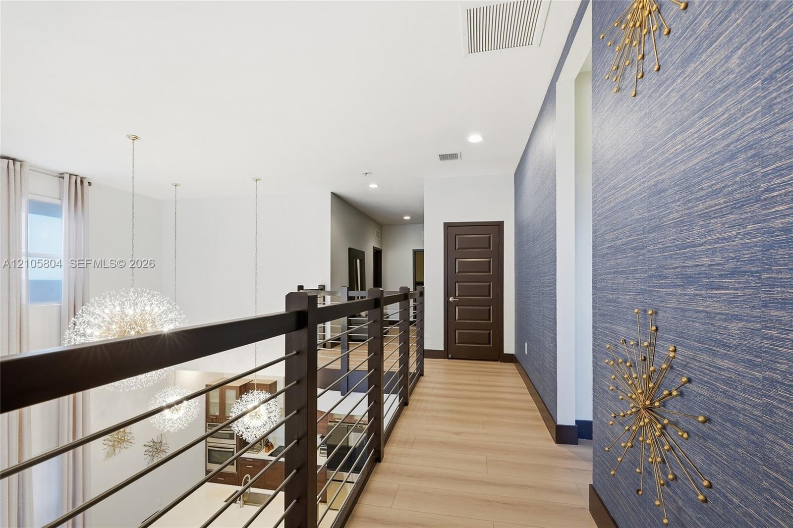 Upper-level walkway featuring wood-finish flooring, a contemporary horizontal cable railing system, textured blue wall covering, and recessed lighting