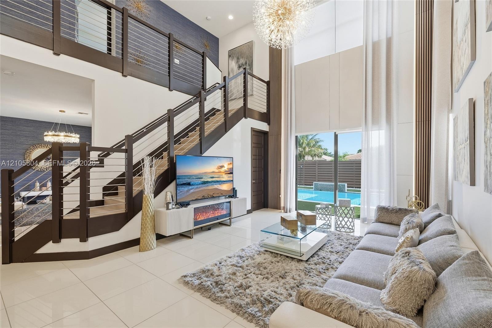 Double-height living area featuring large-format tile flooring, a custom staircase with dark wood-finish treads and a horizontal cable railing system,
