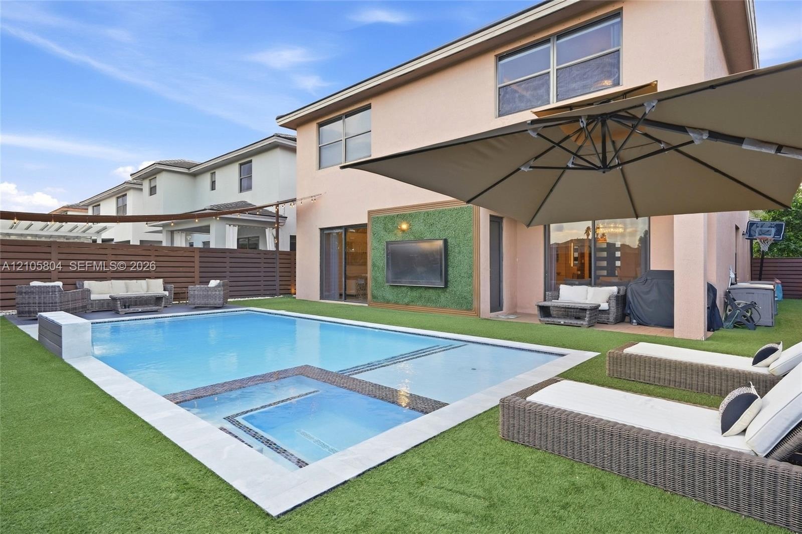 Stucco exterior featuring a pool with an integrated spa, stone-finished coping, artificial turf hardscaping, and a decorative exterior wall panel