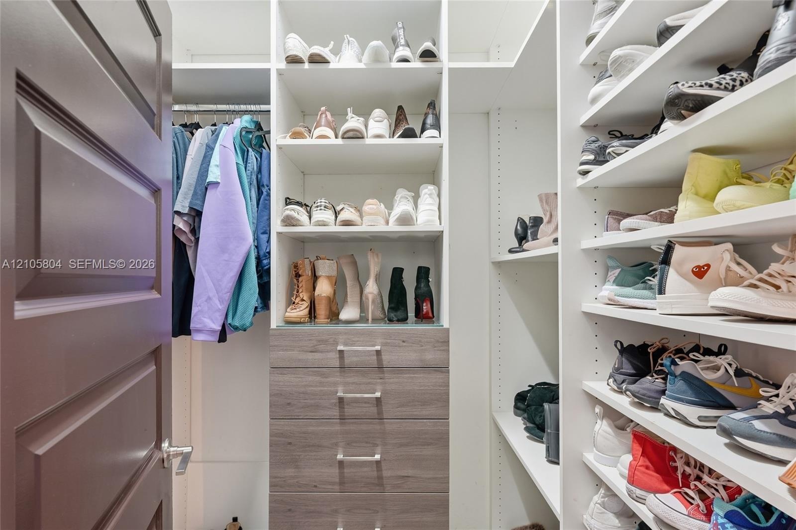 Custom walk-in closet featuring extensive built-in white shelving, integrated wood-finish cabinetry with silver-toned hardware, and a metal clothing r