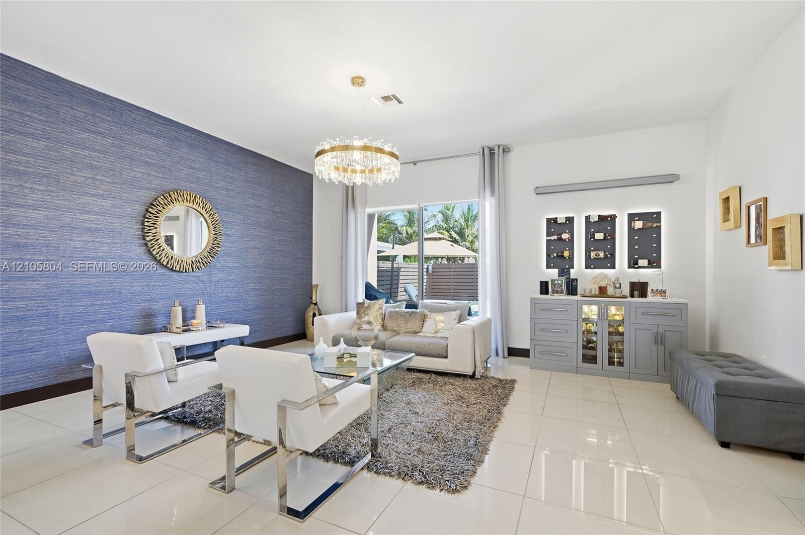 Textured blue accent wall, large-format tile flooring, drum-style crystal chandelier, and built-in cabinetry featuring integrated backlit shelving