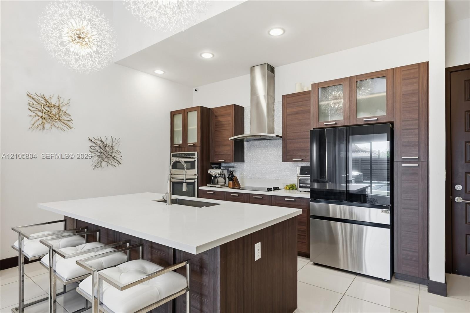 Kitchen featuring custom wood-finish cabinetry, a large central island with a quartz countertop, stainless steel appliances, a glass-tile backsplash, 