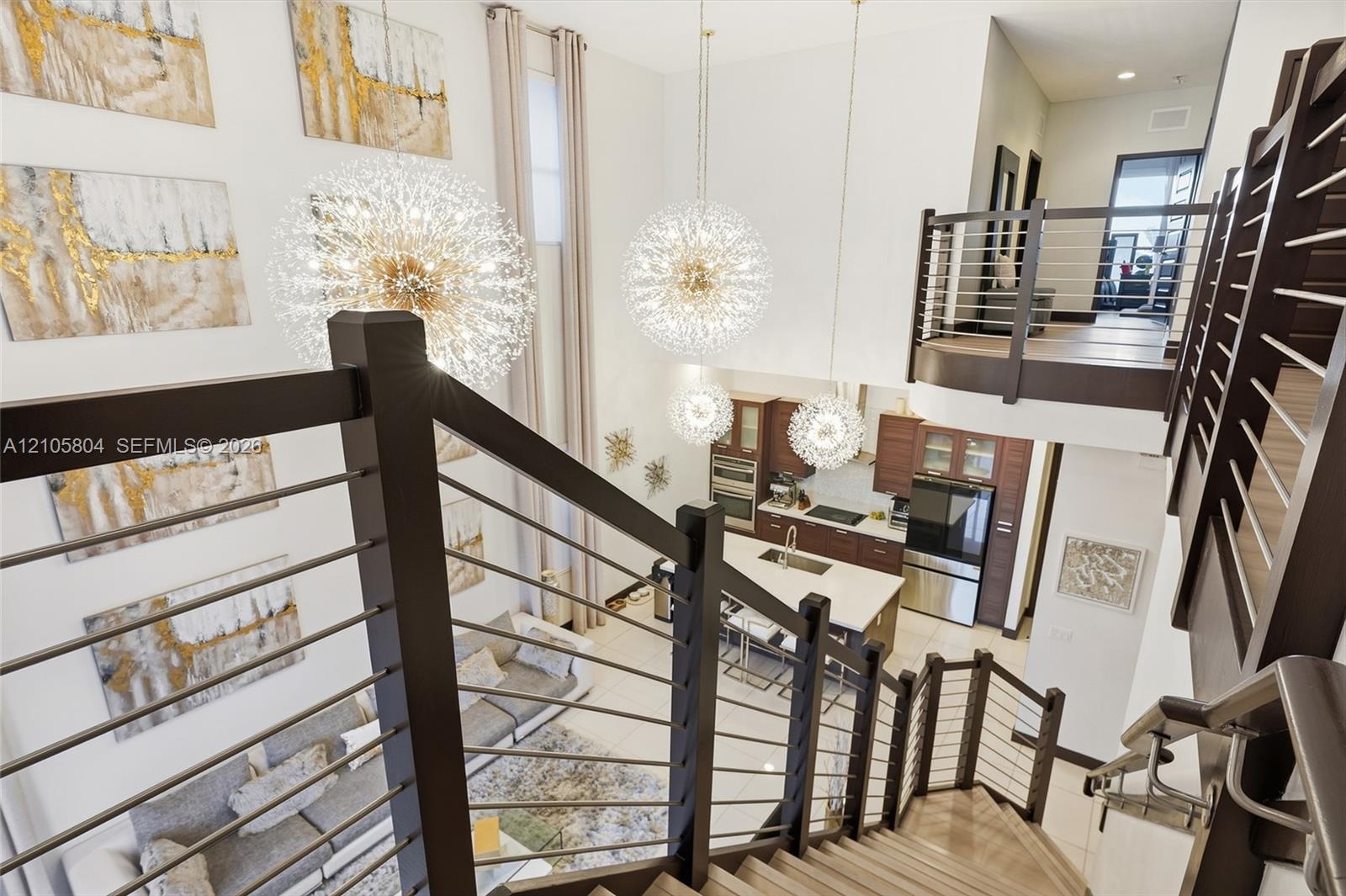 Double-height great room featuring multi-tiered sputnik-style chandeliers, metal cable stair railings, and an open-concept kitchen with built-in cabin
