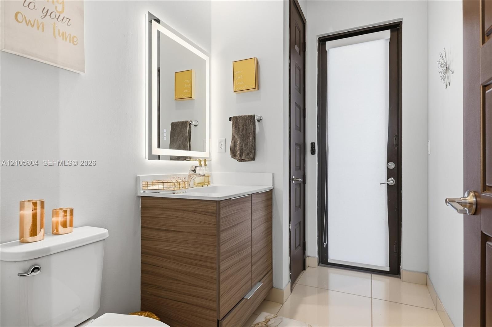 Wood-finish cabinetry, rectangular under-mount sink, integrated LED-backlit mirror, and polished stone-finish countertop
