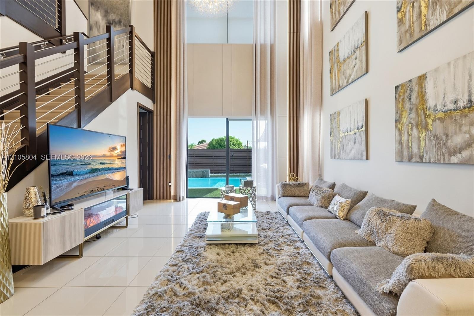 Double-height ceiling, polished tile flooring, staircase featuring dark wood-finish railings with horizontal cable balusters, and floor-to-ceiling gla