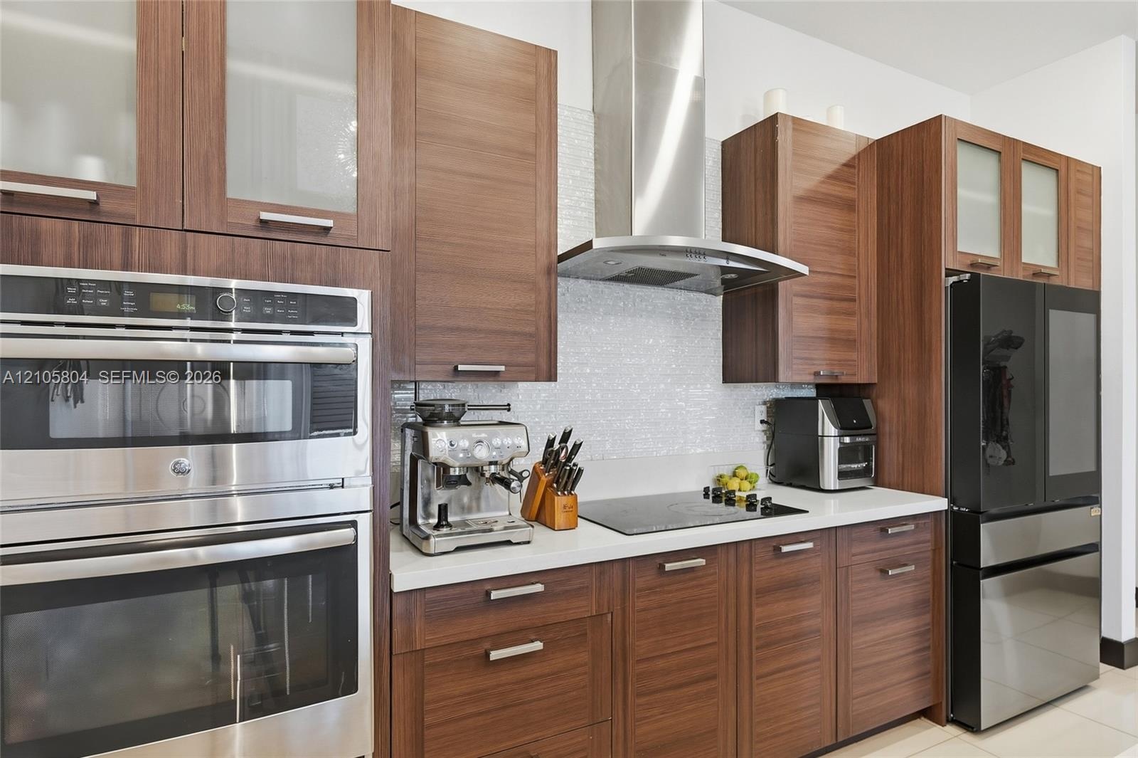 Kitchen featuring wood-finish cabinetry, stone-surface countertops, textured tile backsplash, stainless steel double wall ovens, and a stainless steel