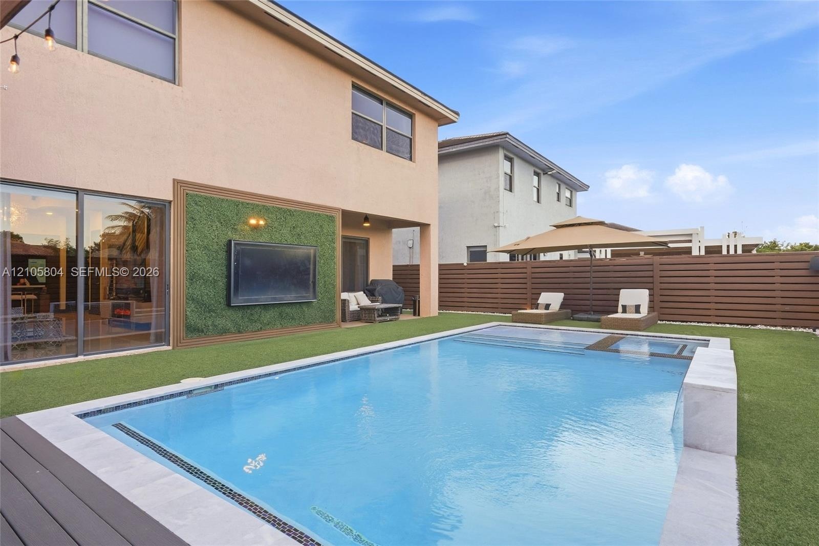Backyard featuring an in-ground swimming pool with a built-in spa, horizontal wood-slat privacy fencing, artificial turf lawn, and an exterior wall fi