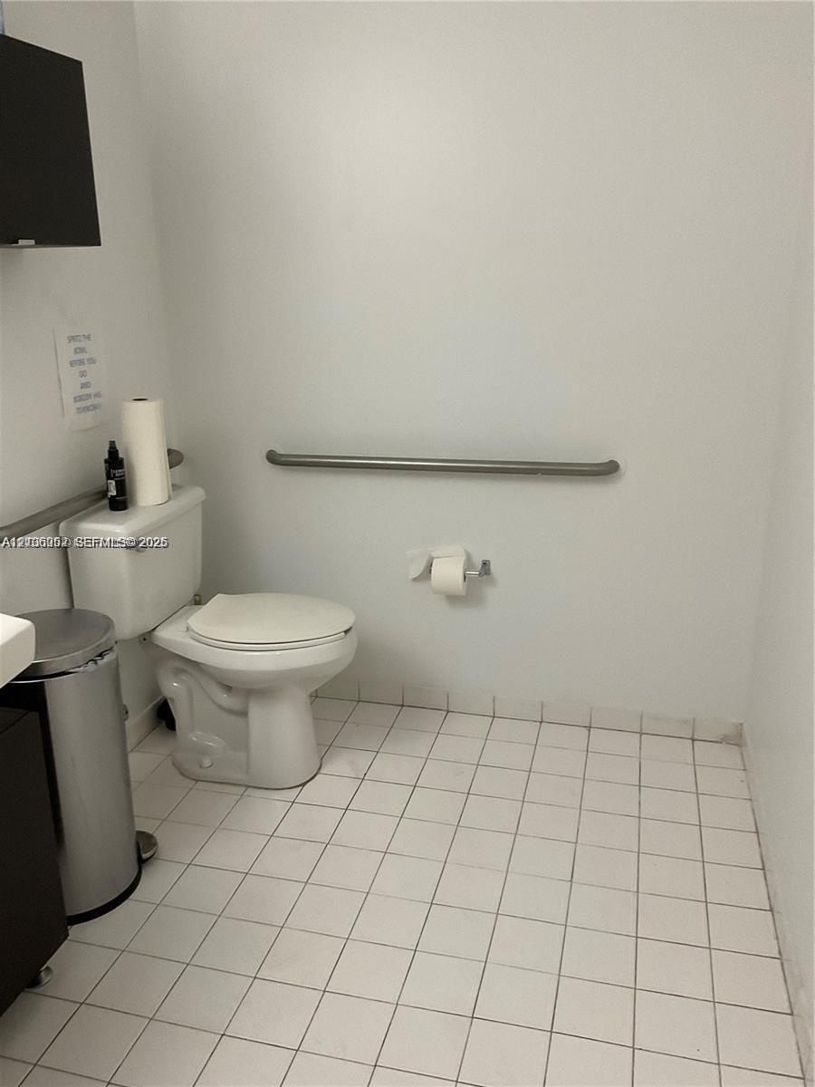 Restroom featuring white ceramic floor tiling, a porcelain toilet, and a mounted stainless steel grab bar