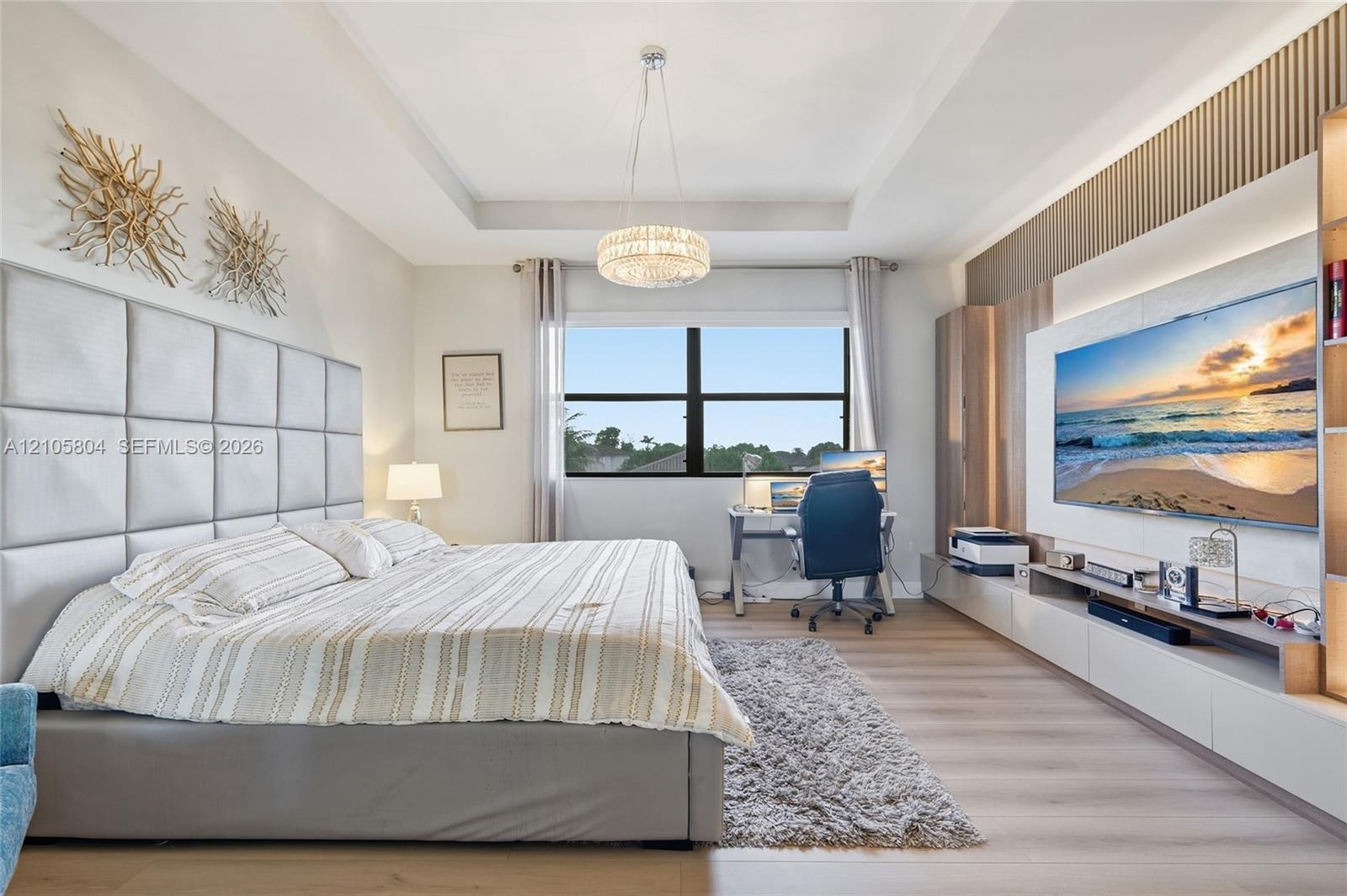 Tray ceiling, custom wood-slat wall feature, built-in media cabinetry, crystal chandelier, and wood-finish flooring