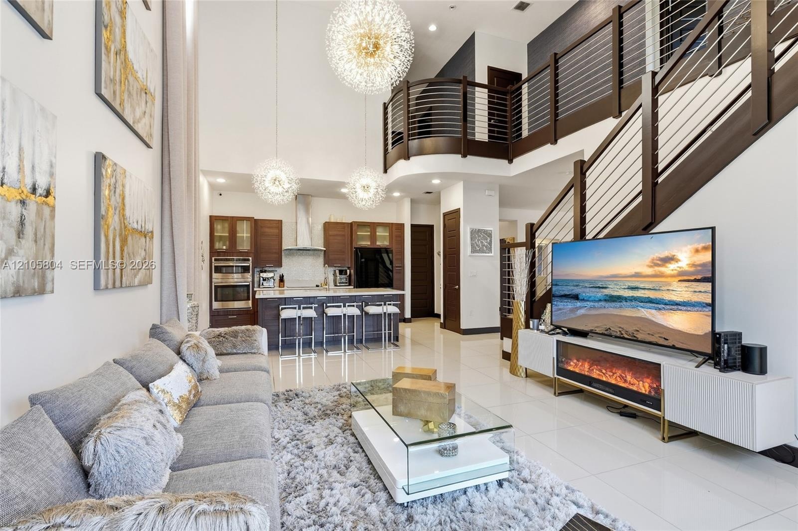 Double-height ceilings featuring tiered spherical pendant lighting, polished stone-finish flooring, and a curved staircase with dark-stained wood hand