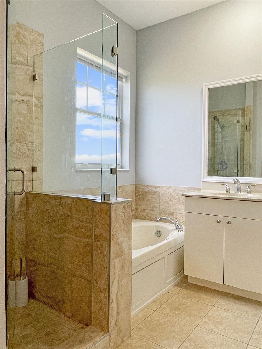 Bathroom featuring a glass-enclosed shower with stone-finish wall tile, a deep soaking tub, and a white vanity with a polished metal faucet