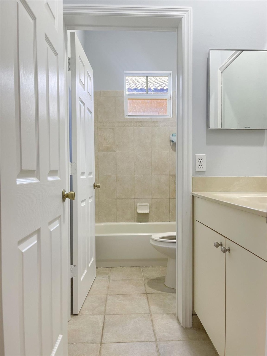 Bathroom featuring a vanity with a neutral-toned countertop, ceramic tile flooring, a tub-shower combination with ceramic wall tile, and a rectangular