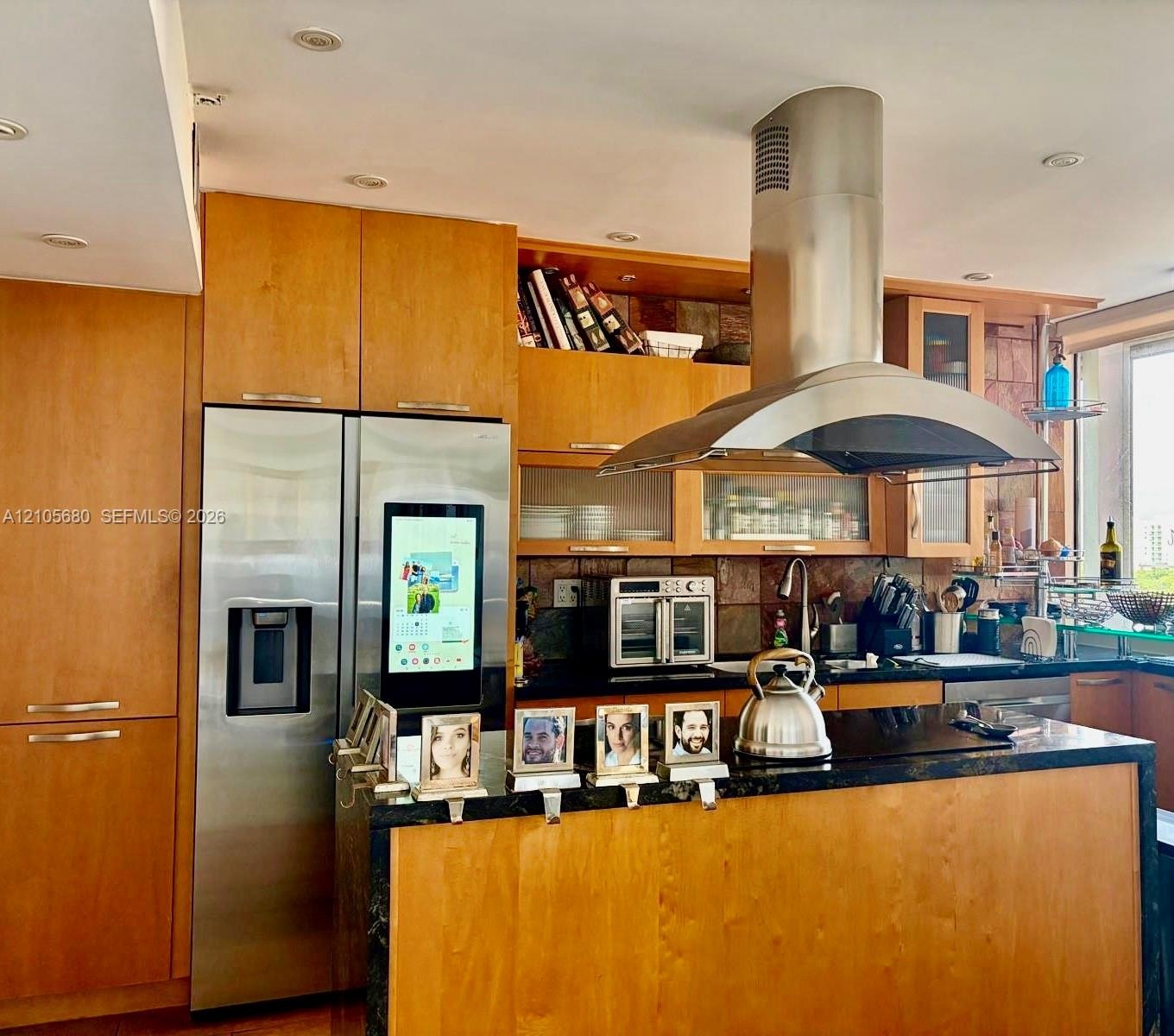 Kitchen featuring custom wood cabinetry, stainless steel appliances, a large center island with a dark stone countertop, and a stainless steel wall-mo