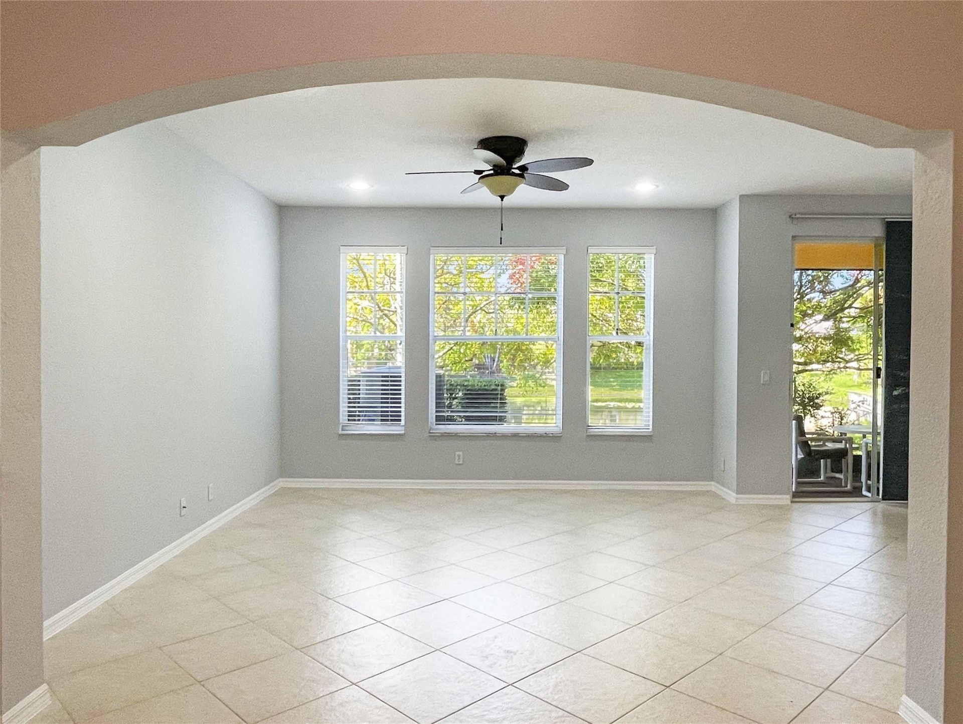 Arched entryway featuring neutral-toned tile flooring, recessed ceiling lighting, a multi-blade ceiling fan, and large windows with grid detailing
