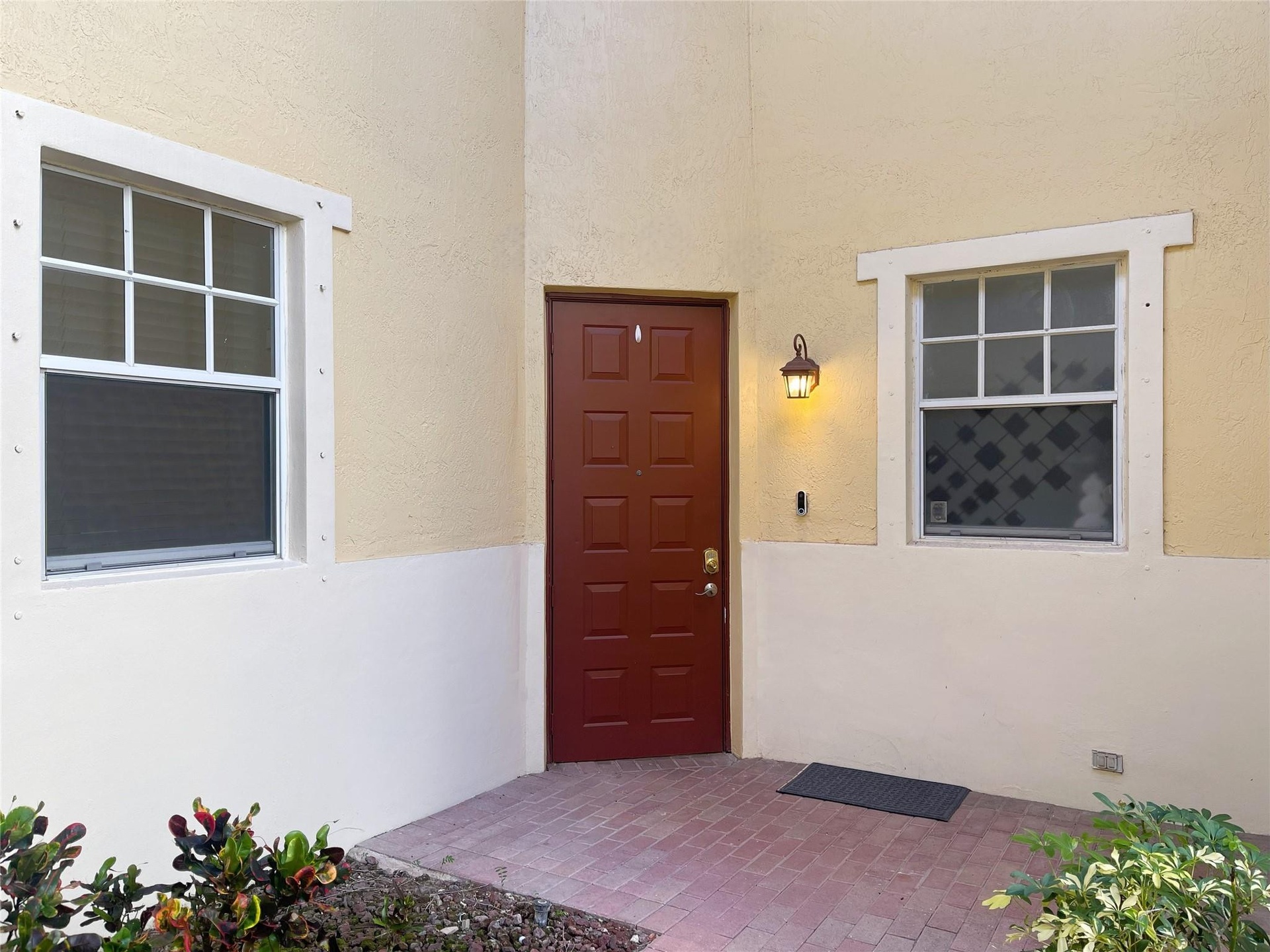 Stucco exterior featuring a dual-tone facade, recessed paneled entry door, brick-paver porch, and multi-pane windows with decorative trim