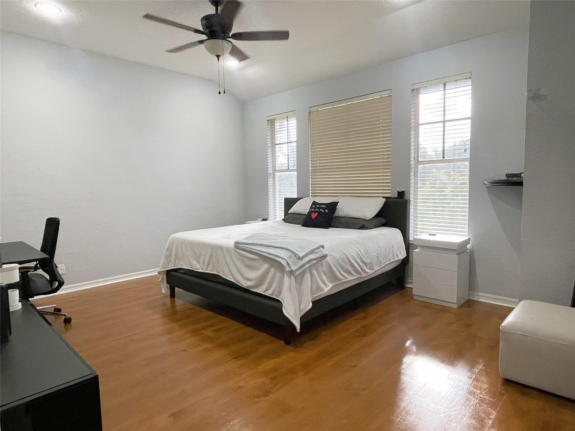 Room featuring vaulted ceilings, wood-finish flooring, a ceiling fan, and three windows with built-in blinds
