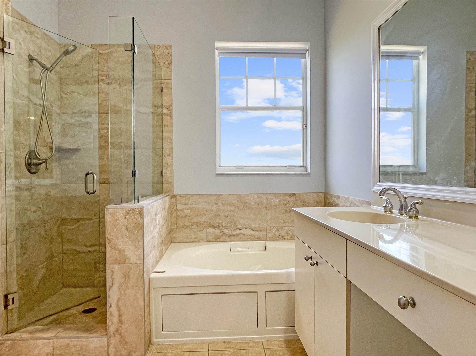 Bathroom featuring a glass-enclosed walk-in shower with stone tile surround, a built-in soaking tub, a single-sink vanity with countertop, and a frame