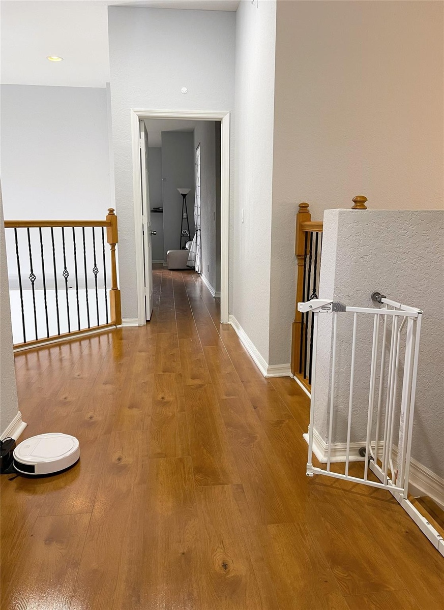 Wood-finish flooring throughout, featuring a staircase railing with wood-capped banisters and black metal balusters
