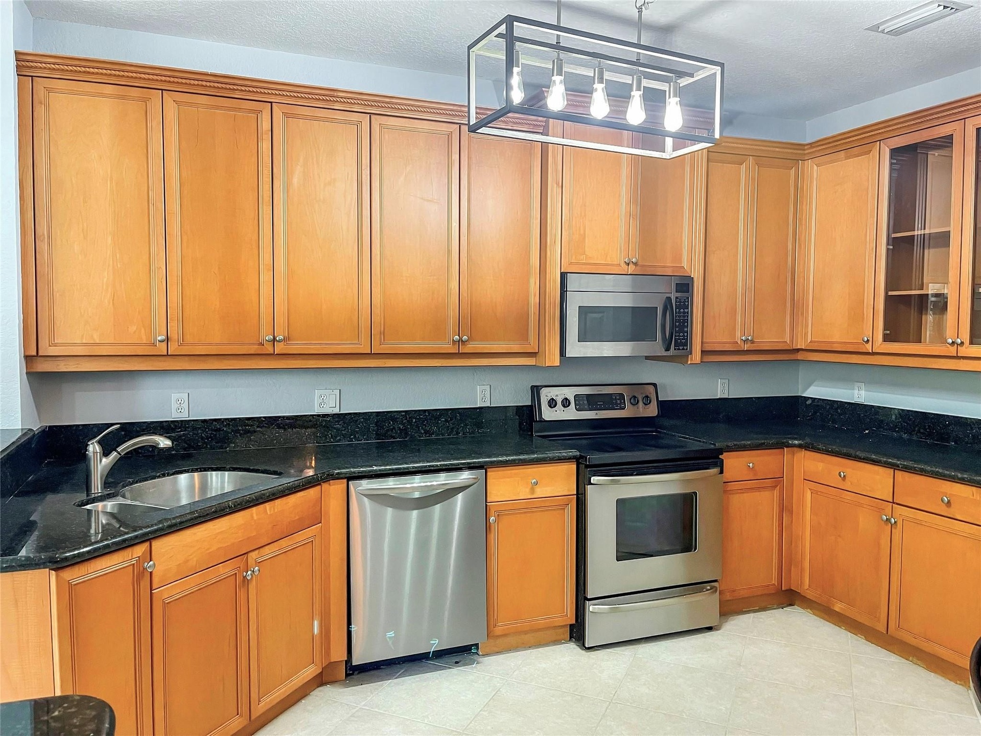 Kitchen featuring wood cabinetry, stone countertops, stainless steel appliances, and a linear open-frame pendant light fixture