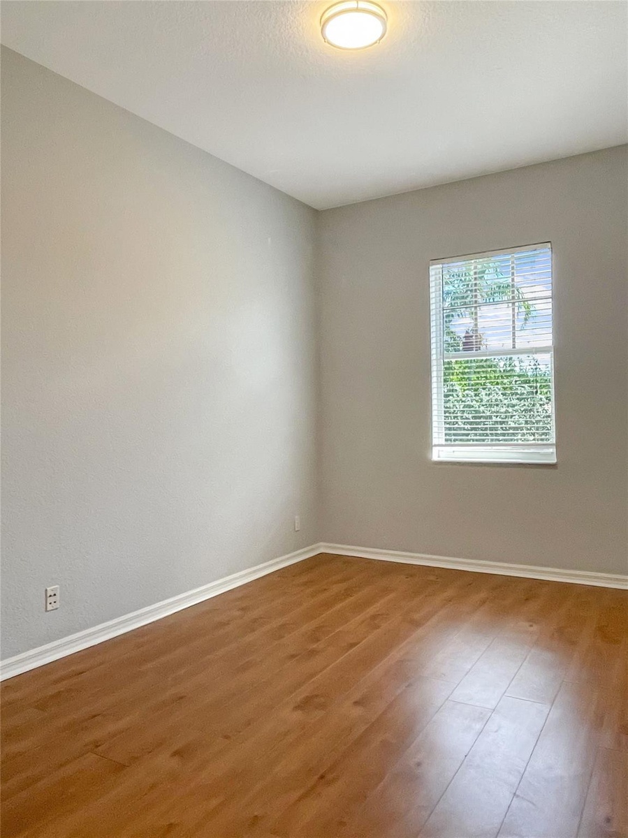 Room featuring wood-finish flooring, neutral wall paint, and a singular window with horizontal blinds, illuminated by a flush-mount ceiling fixture