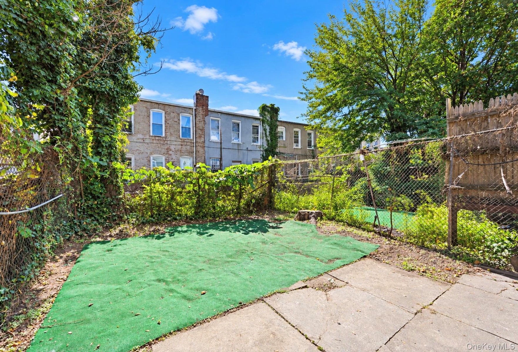 Exterior rear space featuring concrete pavers, synthetic lawn surfacing, and chain-link fencing