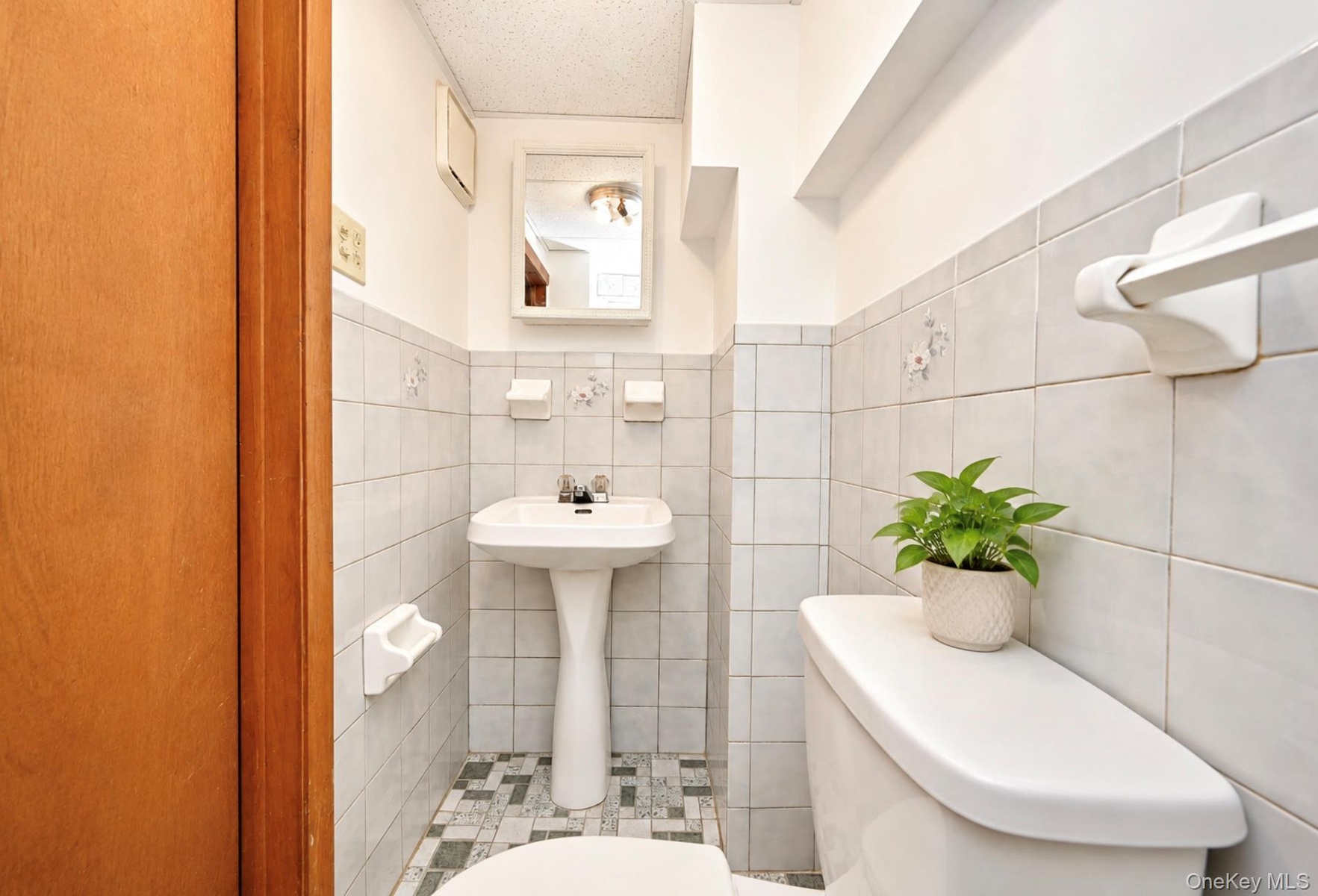 White pedestal sink with a dual-handle faucet, integrated wall-mounted medicine cabinet, square ceramic wall tiling, and mosaic-patterned flooring