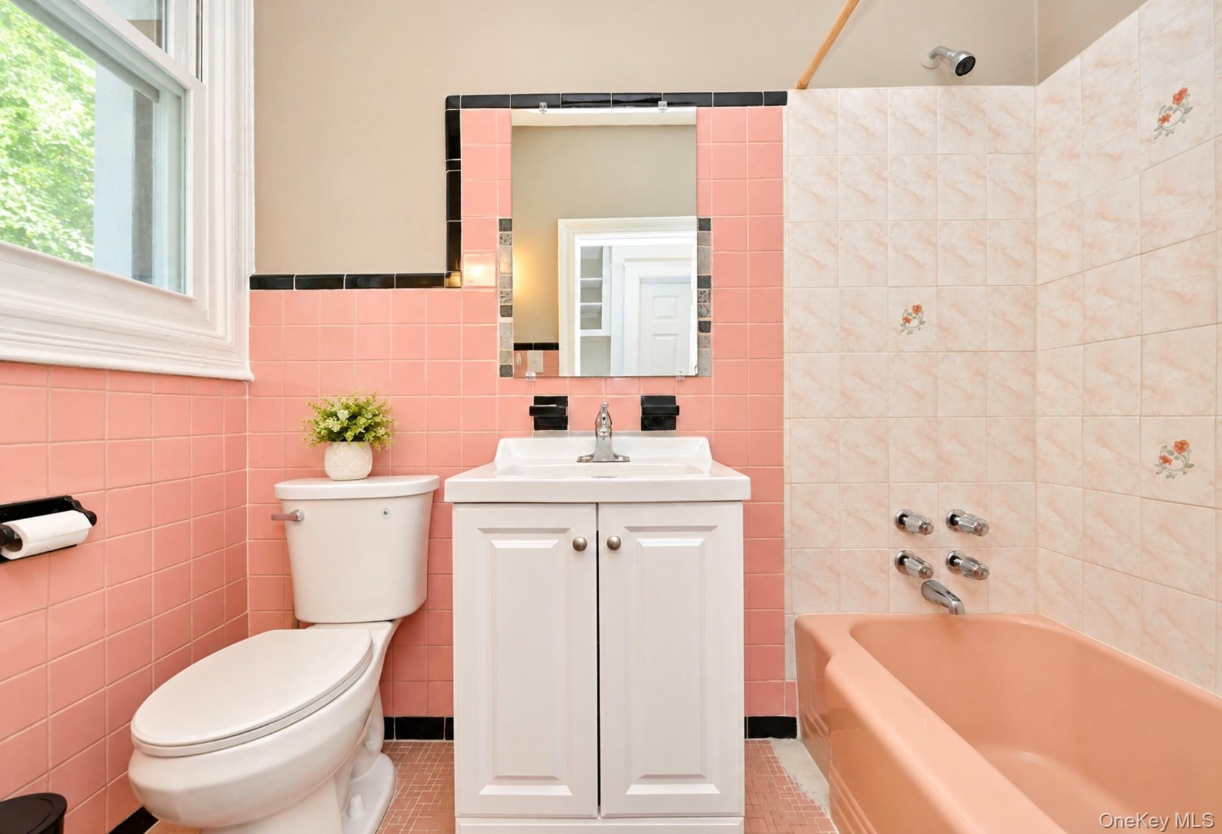 1st. Floor: Bathroom featuring pink square wall tiles with black trim, a white vanity cabinet with an integrated basin, a porcelain soaking tub, and a