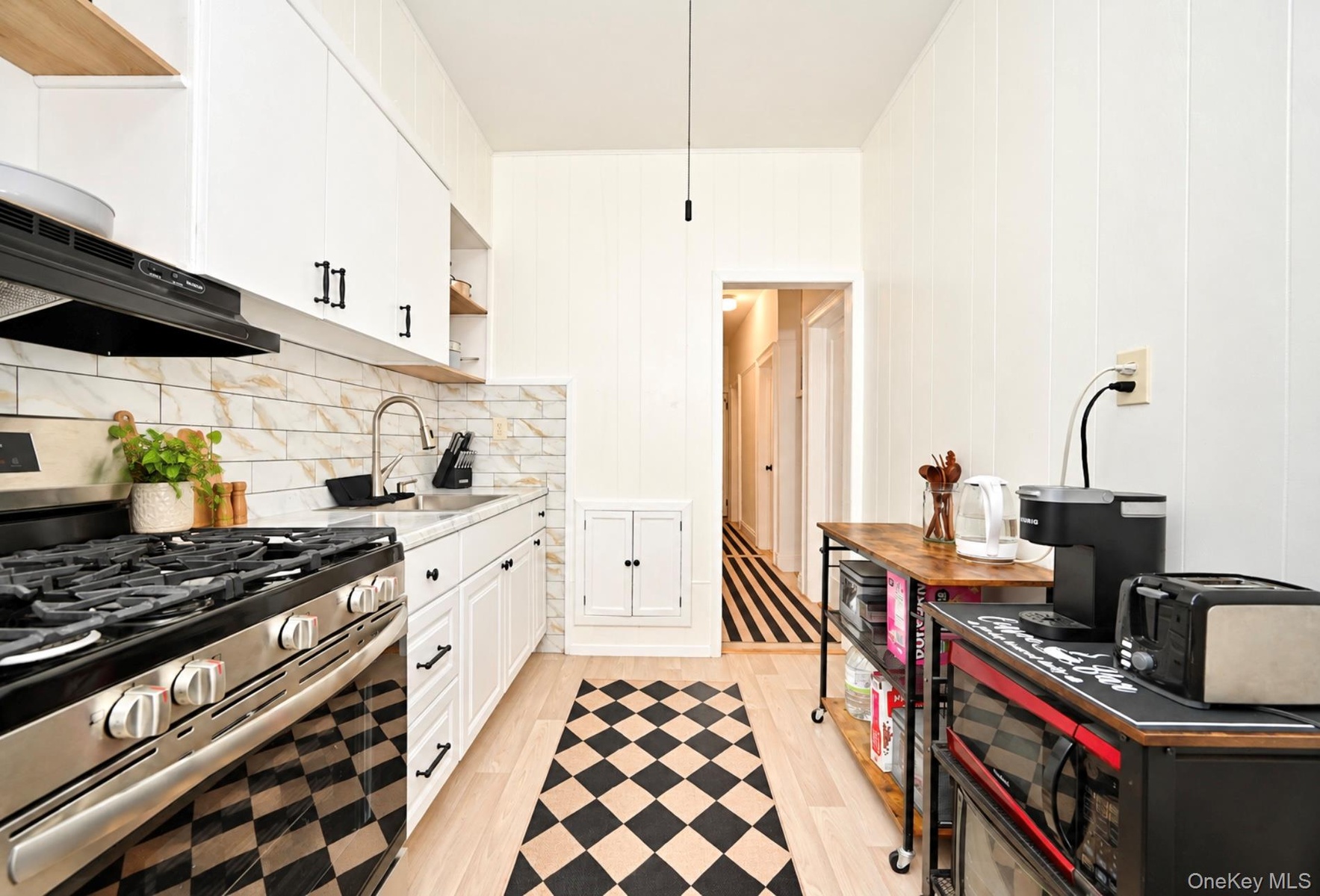 1st Floor: Kitchen featuring white cabinetry with matte black hardware, stainless steel gas range, stone-tiled backsplash, and wood-finish flooring
