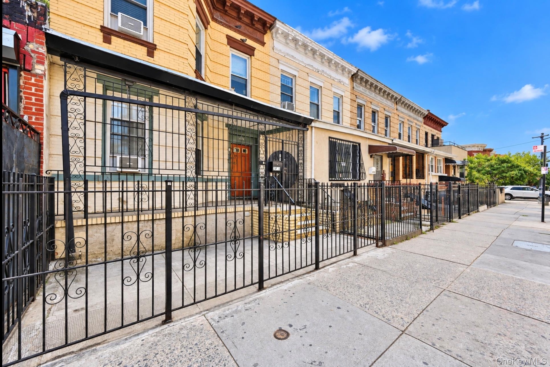 Brick townhouse exterior featuring a warm-toned masonry facade, decorative wrought iron security fencing, a multi-pane wood entry door, and ornate cor