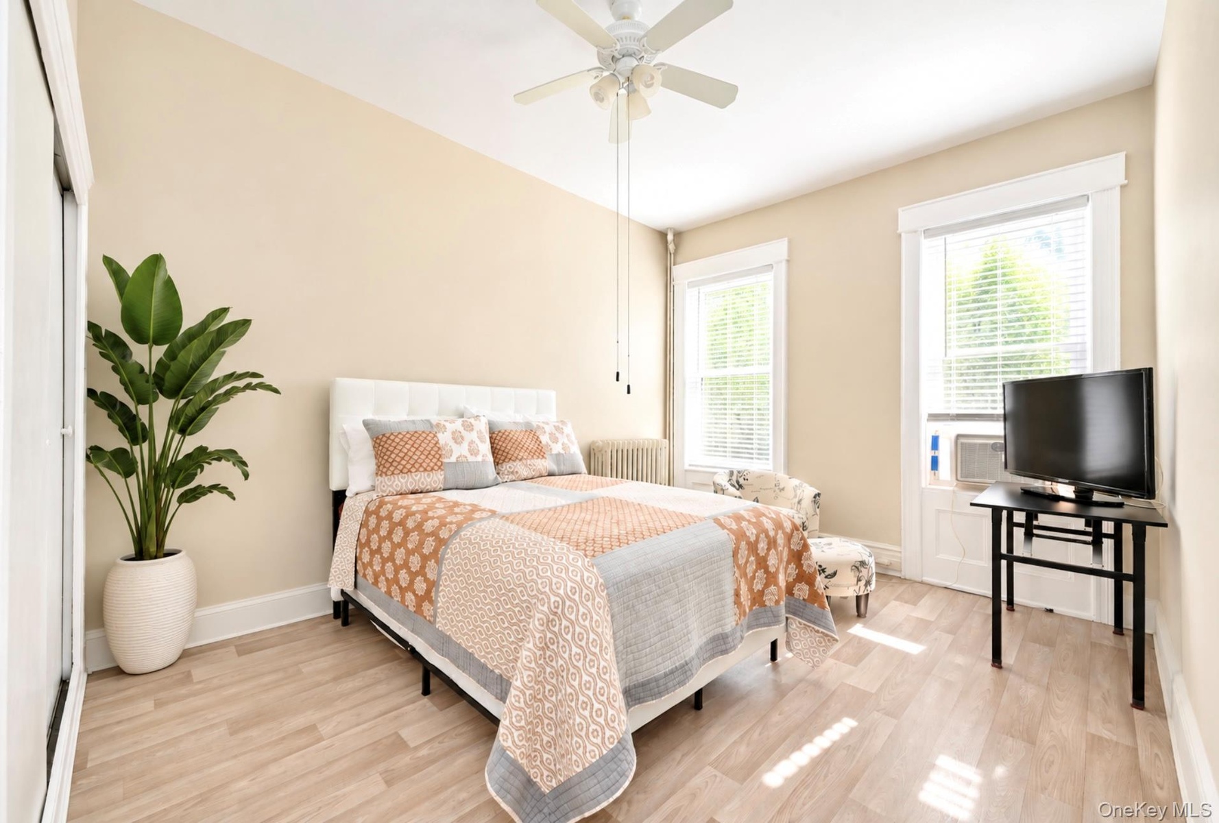 2nd. Floor: Light-filled room featuring wood-finish flooring, dual windows with wide white trim, a ceiling fan, and a radiator
