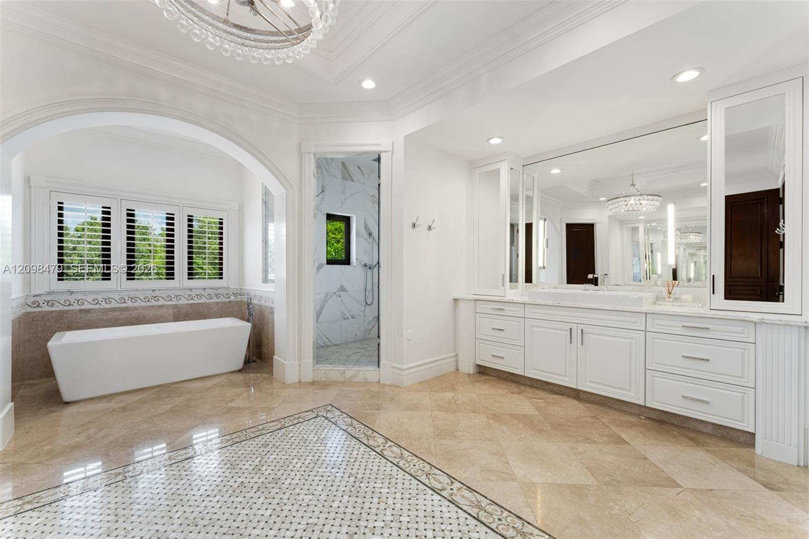 Freestanding soaking tub, walk-in shower with marble-finish walls, dual vanity with extensive storage, full-height wall mirror, and chandelier lightin