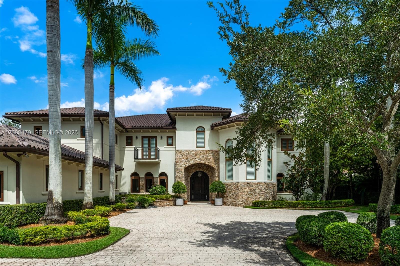 Mediterranean Revival architectural style with a tile roof, stone accents, and a paved circular driveway
