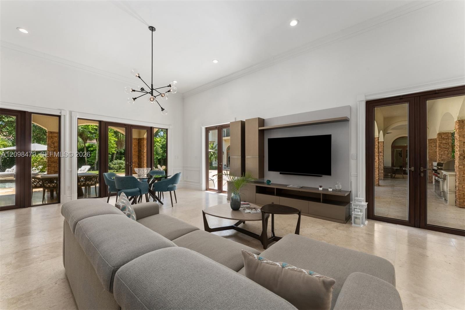 High ceilings with crown molding, stone-finish flooring, multiple sets of glass French doors, and an open-concept living and dining area